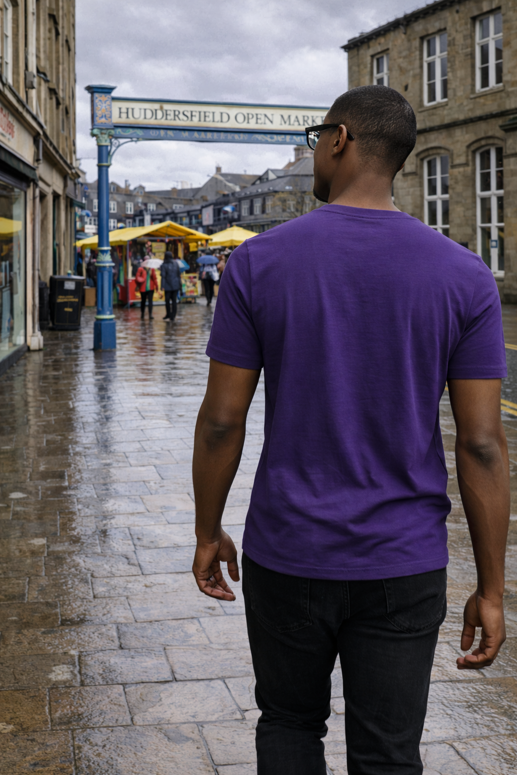 Man in a purple shirt walking on a wet street near Huddersfield Open Market sign in the background