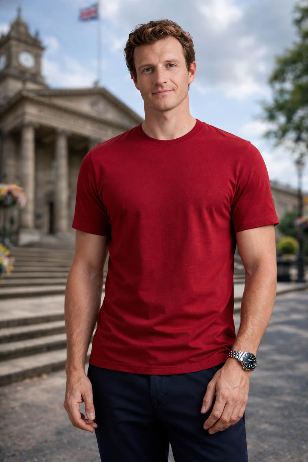Man wearing a red t-shirt standing outdoors with a building and clock tower in the background
