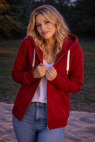 Woman wearing a red hoodie and blue jeans standing outdoors.