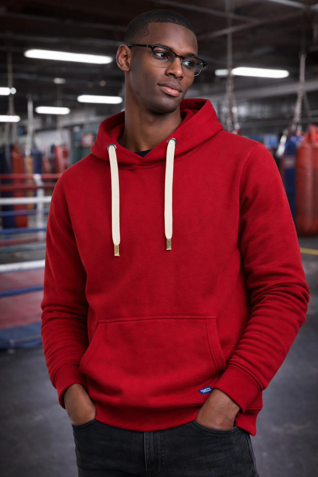 Man wearing a red hoodie in an indoor setting with boxing ring equipment.