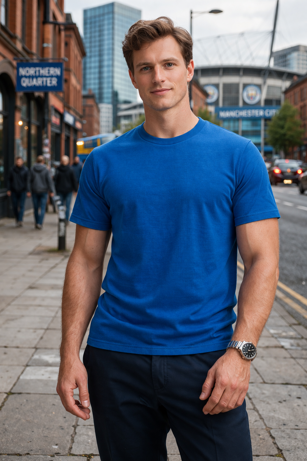 Man wearing a blue t-shirt standing on a city street with buildings and a sign in the background.