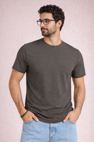 Man wearing a dark gray t-shirt and light blue jeans against a plain background